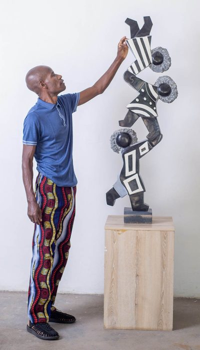 Zimbabwean artist adjusting sculpture on platform